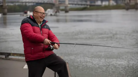Happy Asian man in a red jacket fishing off a dock in the Willamette River